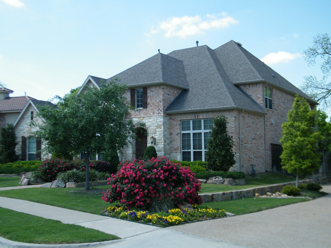 A large house with a tree and blooming bushes in the front yard, courtesy of St. Charles tree service